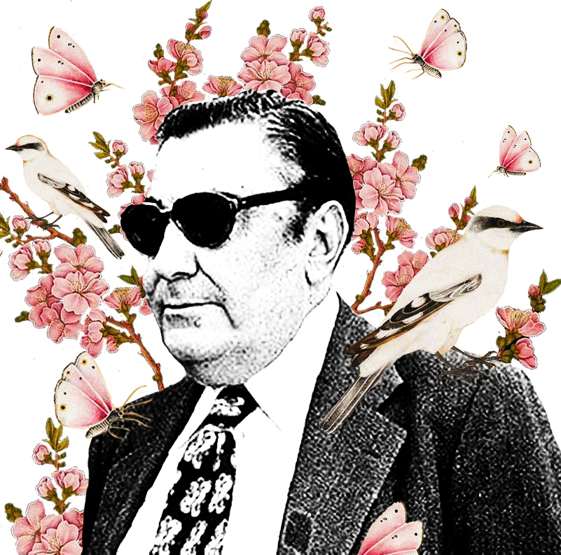 A man with sunglasses and a suit standing in front of flowers.